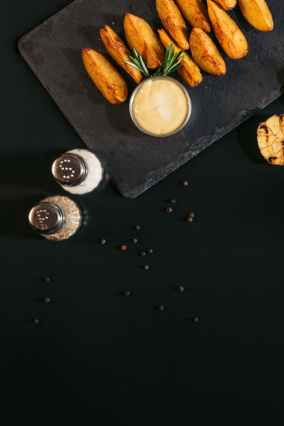 κάτοψη του μπαχαρικά, πατάτες φούρνου με σως και ψητό σκόρδο σε μαύρο - Φωτογραφία, εικόνα