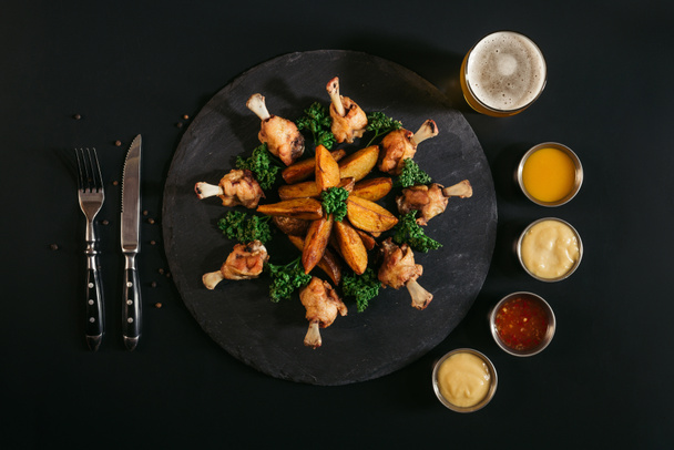 グルメ焼き鶏、ビールのグラス、ナイフとフォークをジャガイモと黒のさまざまなソース  - 写真・画像