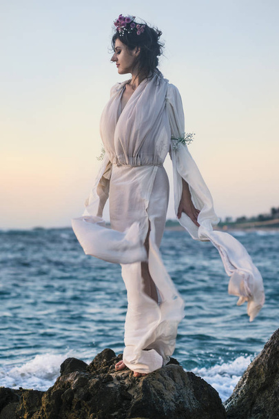 schöne Frau in einem weißen Kleid, die am Rande des Strandes während eines Sonnenuntergangs spaziert. Horizontlinie - Foto, Bild