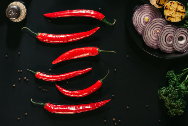 το Top view κόκκινες πιπεριές τσίλι, πιπέρι, κρεμμύδι κομμένο σε φέτες και ψητό σκόρδο σε μαύρο - Φωτογραφία, εικόνα