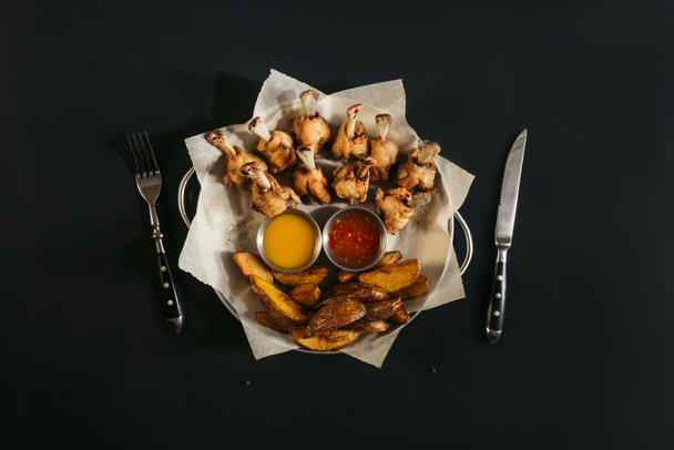 top view of delicious baked potatoes with sauces and roasted chicken wings on black - Foto, Imagen