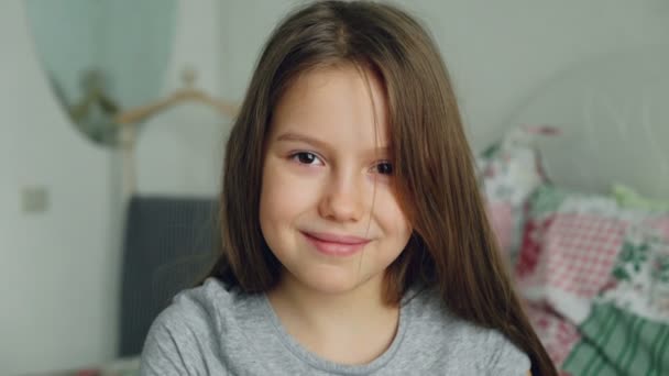 Close-up portrait of little cute girl looking at the camera and smiling kindly in bedroom at home - Video