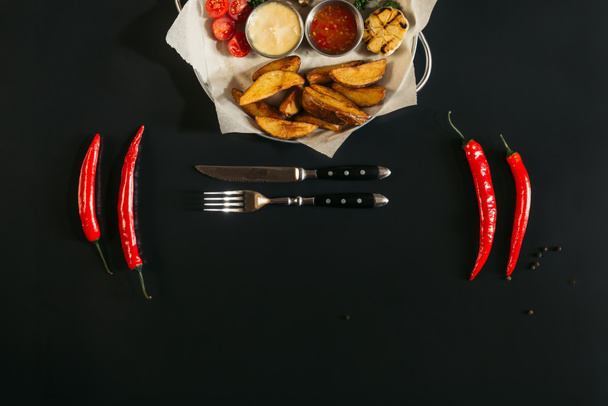νόστιμες πατάτες φούρνου με σάλτσες, ποτήρι μπύρα, πιπεριές τσίλι και πιρούνι με μαχαίρι σε μαύρο  - Φωτογραφία, εικόνα