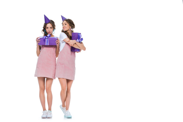 krásná mladá dvojčata v narozeninové čepice drží dárky izolované na bílém - Fotografie, Obrázek