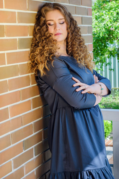 nice woman with chic curly hair stands near a brick wall in the  - Fotoğraf, Görsel