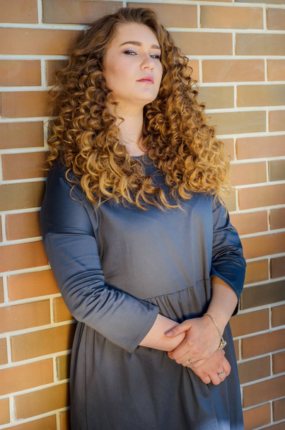 nice woman with chic curly hair stands near a brick wall in the  - 写真・画像