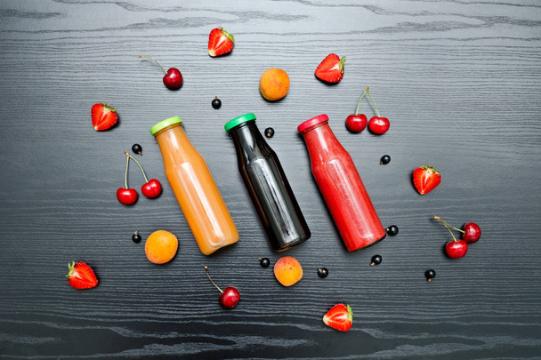 Three bottles of juice and fruits. Black wooden background. - Φωτογραφία, εικόνα