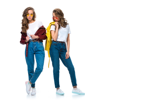 mooie stijlvolle tweeling poseren in lederen jassen en zonnebrillen geïsoleerd op wit - Foto, afbeelding