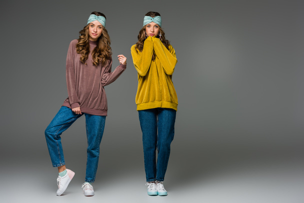 attractive young twins in sweaters looking at camera on grey - Photo, Image