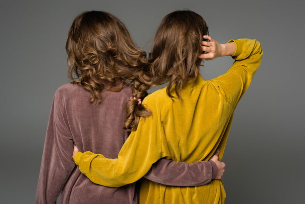 Rückansicht von Zwillingen, die sich mit Haaren in einem Zopf umarmen, isoliert auf grau - Foto, Bild