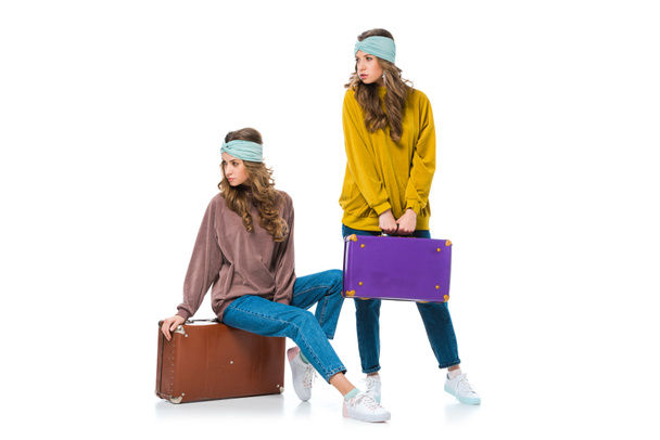 привлекательные близнецы в стиле ретро с дорожными сумками, смотрящими вдаль на белом
 - Фото, изображение