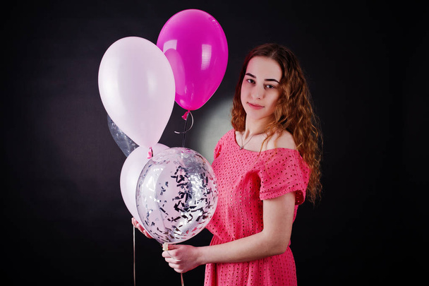 Jong meisje in de rode jurk met ballonnen tegen zwarte achtergrond o - Foto, afbeelding