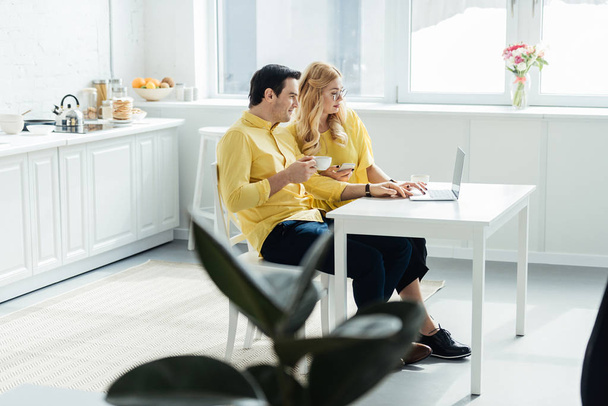 Άνδρας και γυναίκα πίνοντας τον καφέ και να εργάζονται για το laptop στην κουζίνα - Φωτογραφία, εικόνα