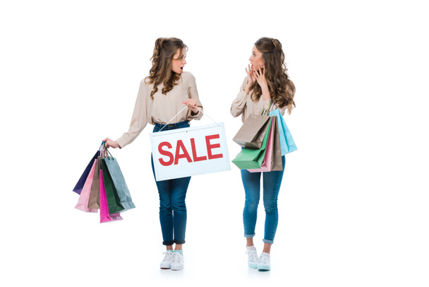 überraschte junge Zwillinge mit Verkaufsschild und Einkaufstüten auf weißem Grund - Foto, Bild