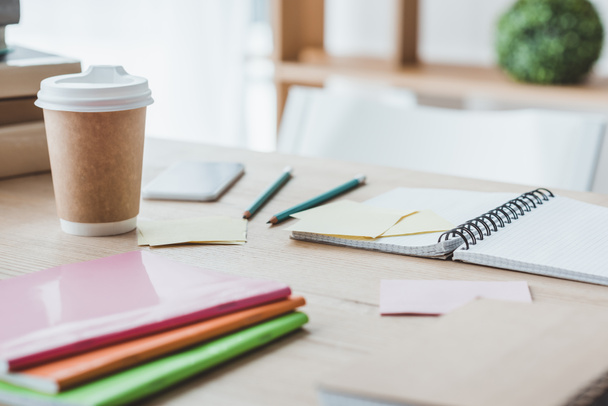 zbliżenie na edukacyjne Notesy i jednorazowe filiżankę kawy na stole  - Zdjęcie, obraz