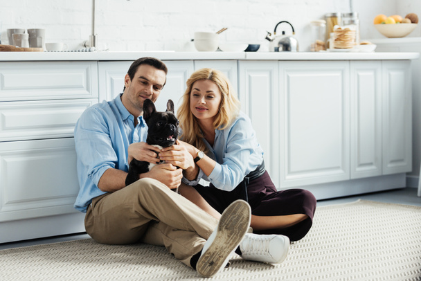 Hymyilevä pari silitti ranskalaista bulldoggia keittiön lattialla
 - Valokuva, kuva