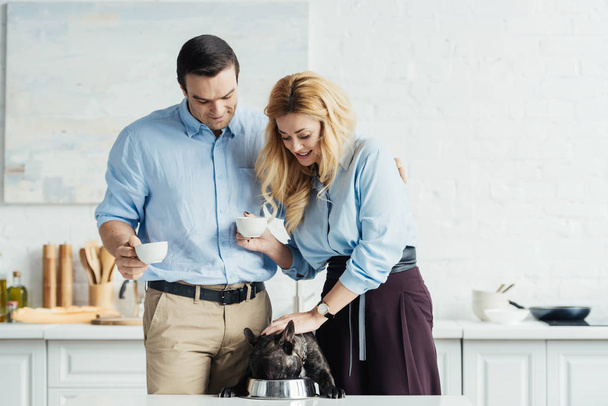 Couple drinking coffee and feeding french bulldog on kitchen table - Foto, Imagen