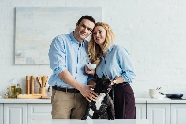 Couple souriant caressant leur chien frenchie sur la table de cuisine
 - Photo, image
