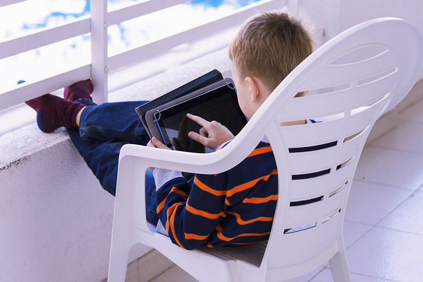 carino bambino sta giocando nel tablet sul balcone su una vacanza in primavera
 - Foto, immagini