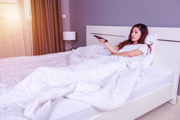 woman lying on a bed with remote control and watching television - Foto, Imagem