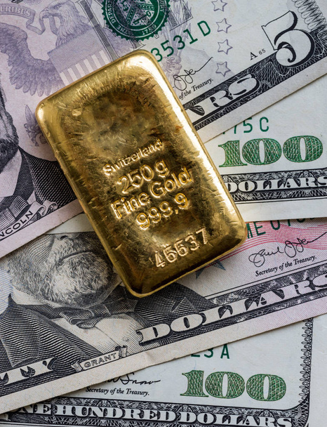 Cast gold bar weighing 250 gram against the background of dollar bills.  - Photo, Image