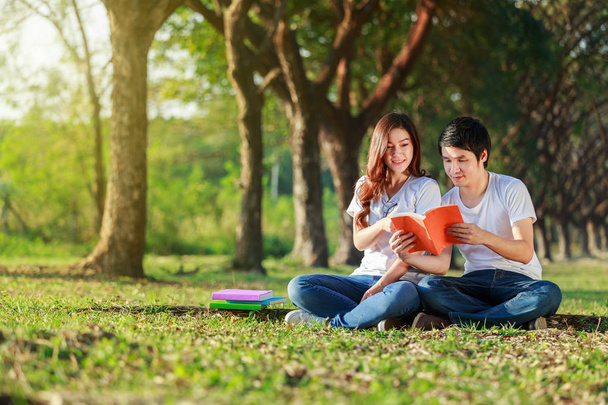 man and woman sitting and reading a book in park - 写真・画像