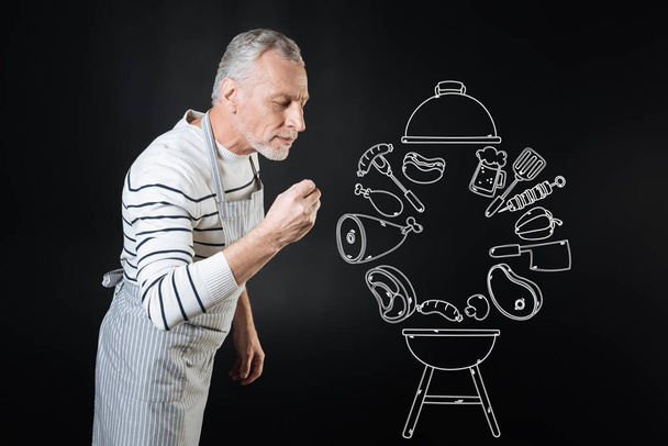 Calm professional cook smelling the dish while cooking it - Foto, afbeelding
