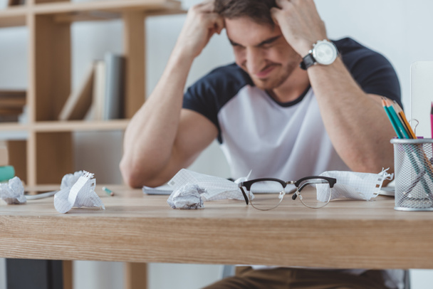 depressed student studying at table with crumpled papers and eyeglasses - Photo, Image