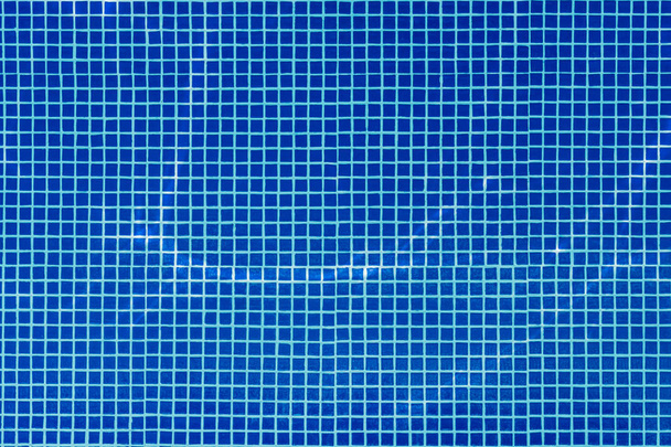 View over water surface of swimming pool with blue mosaic tiles design on floor, water in motion - Photo, image