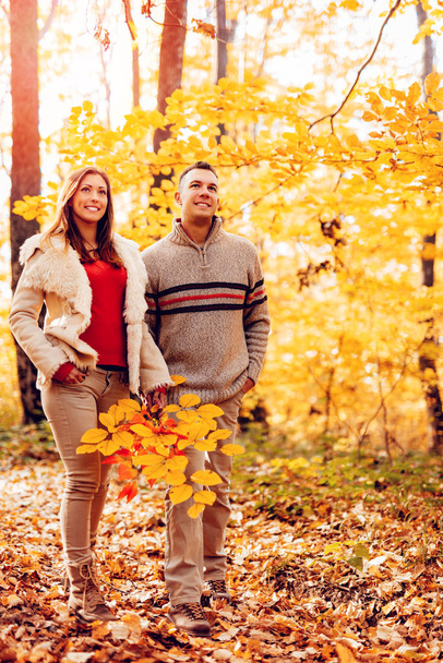 Hermosa pareja sonriente caminando en un bosque soleado en colores otoñales
. - Foto, imagen