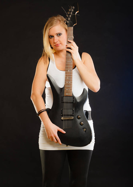 Blonde woman holding electric guitar, black background - Foto, Imagen