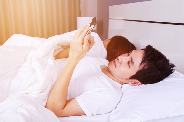 man using his mobile phone in bed while his wife is sleeping nex - Valokuva, kuva