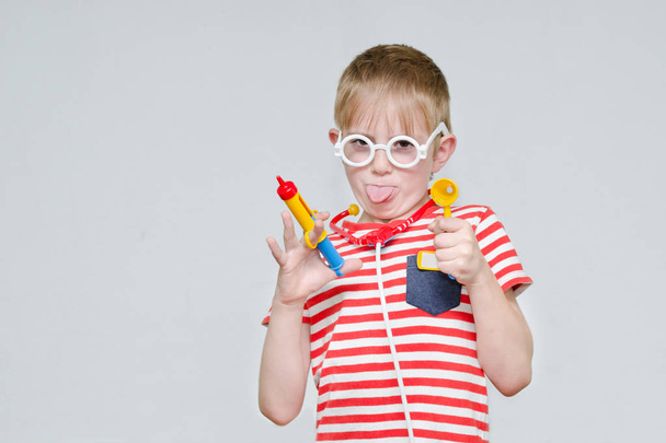 Funny boy playing doctor. Toy syringe, glasses and phonendoscope - Photo, Image