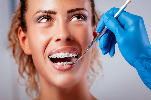 Hammaslääkäri tarkistaa hammasraudat hammaspeilin kanssa nuorella hymyilevällä naispotilaalla
.  - Valokuva, kuva