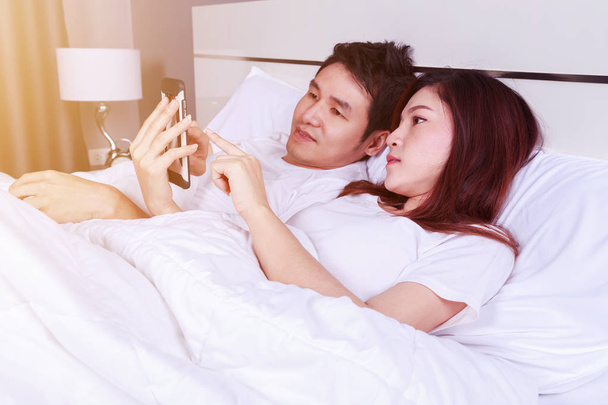 young couple using mobile phone on bed in bedroom - Foto, Bild