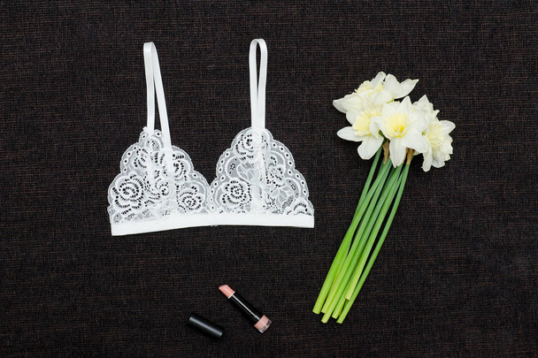 White lace bra and bouquet of daffodils on a black background. - Photo, Image