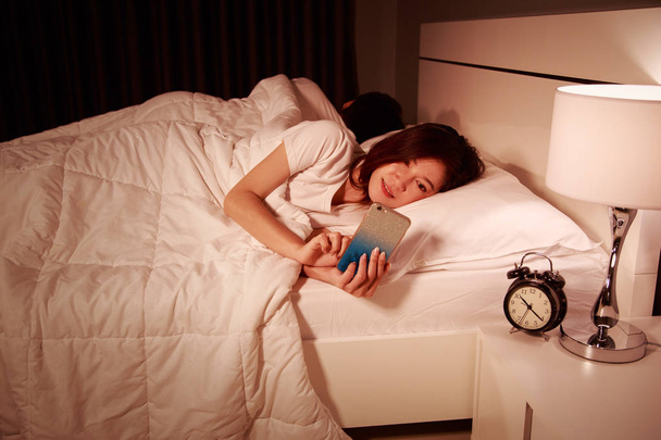 femme utilisant son téléphone portable dans le lit la nuit tandis que son mari i
 - Photo, image