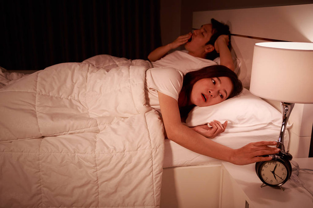 unhappy couple being awakened by an alarm clock in bedroom in mo - Photo, Image