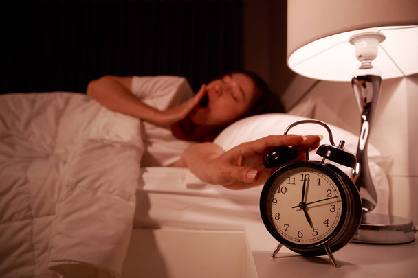 сонная женщина в постели с закрытыми глазами протягивая руку к будильнику clo
 - Фото, изображение