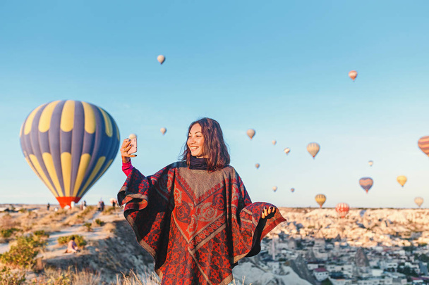 traveler enjoying valley view and making selfie on a phone with wonderful balloons flight over Cappadocia valley in Turkey - Foto, Imagen