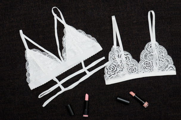 Two white lace bra and lipsticks on a black background. - Photo, Image
