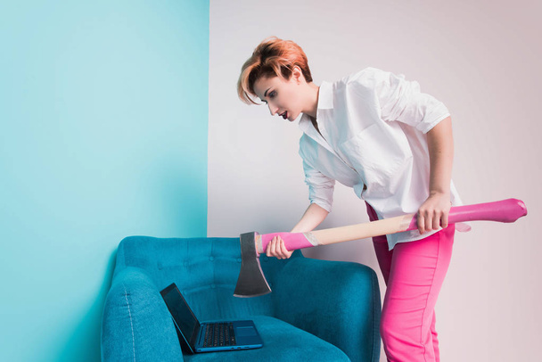Angry furious businesswoman girl with an ax smashes a laptop, screaming. Negative human emotions, facial expressions, feelings, aggression, anger management issues concept - Photo, image
