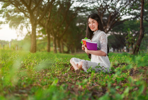 young woman holding a book in park - 写真・画像