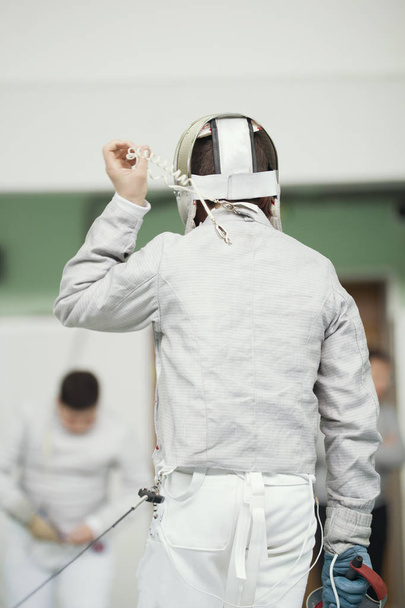 Espalda de joven esgrimista en traje blanco y máscara protectora
 - Foto, imagen