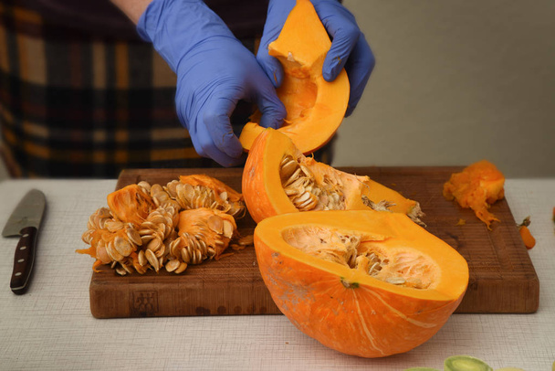 preparing pumpkin, woman's hands with blue rubber gloves remove the seeds from the fruit - Zdjęcie, obraz
