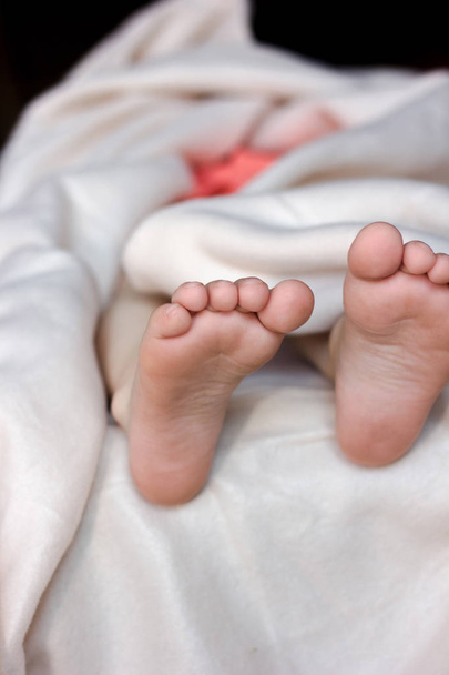 Bambino sdraiato nel letto e piede con dita dei piedi e tacchi su coperta bianca
 - Foto, immagini