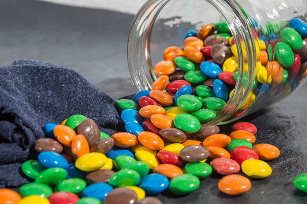delicious colorful chocolate candies in spilled glass jar - Photo, Image