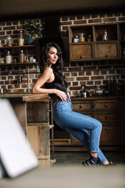 Beautiful brunette in the kitchen, modern housewife, fashion, wooden brown furniture, dressed in blue jeans and a blue shirt - Photo, image