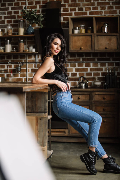 Beautiful brunette in the kitchen, modern housewife, fashion, wooden brown furniture, dressed in blue jeans and a blue shirt - Photo, Image
