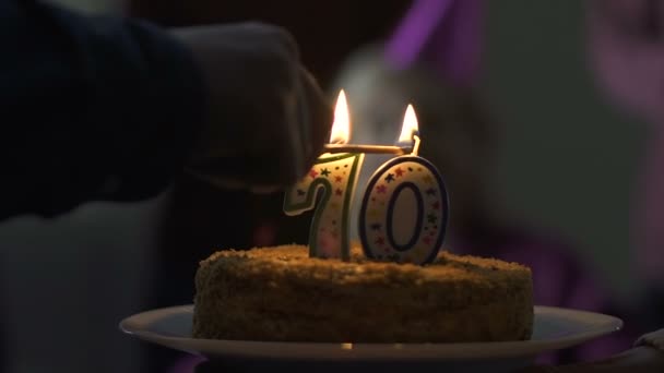 Happy 70 years old woman blowing out candles on birthday cake at home party - Felvétel, videó